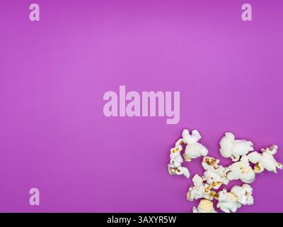 White salted popcorn scattered on purple background right corner bottom view from above. High quality photo Stock Photo