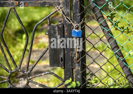 A small blue padlock with a key hanging on a metal fence, a closed garden gate Stock Photo