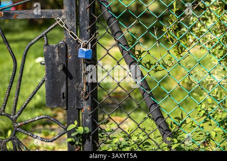 A small blue padlock with a key hanging on a metal fence, a closed garden gate Stock Photo