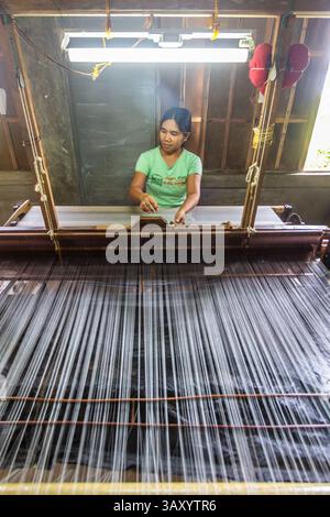 A young Filipina artisan weaves piña fibers on a traditional loom in ...