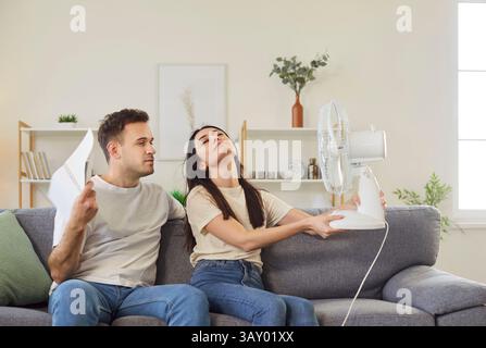 Family couple, woman, man enjoying freshness using electric ventilator, cooler to enjoy fresh air  Stock Photo