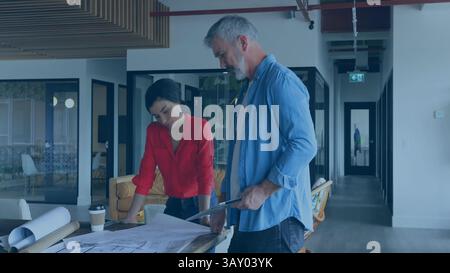 Two architects are collaborating over plans in flat architecture office, with tubes and coffee Stock Photo