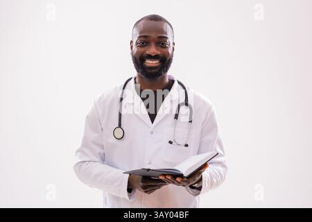 Portrait of successful and confident African American doctor who is holding notepad, smiling and looking at camera on gray background. Stock Photo
