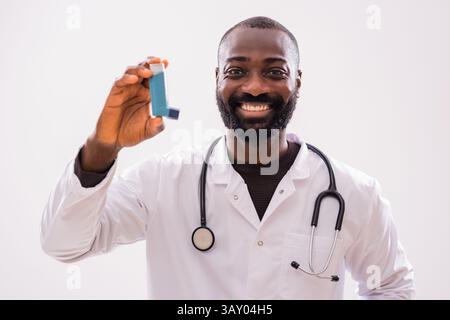 Portrait of happy African doctor in medical uniform who is showing inhaler and promoting respiratory care. Stock Photo