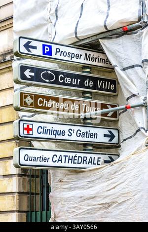 Road direction signs poking out from building covered in scaffolding and taupaulins - Tours, Indre-et-Loire (37), France. Stock Photo