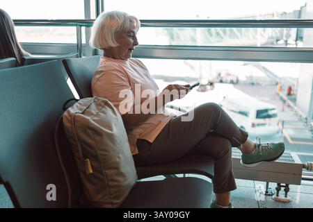 Senior woman waiting at the airport terminal while using her smartphone Stock Photo