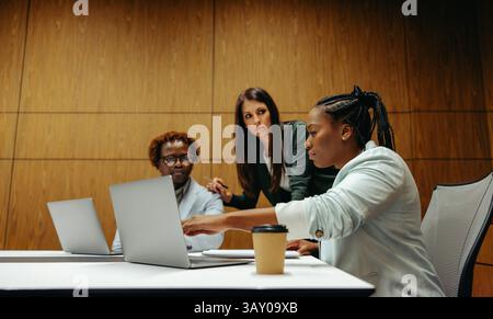 A professional business team engaged in a meeting, collaborating on strategies at an audit firm. Three diverse team members are focused on laptops, ex Stock Photo