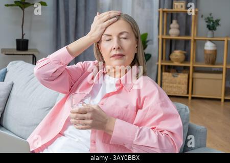 Feeling unwell. Woman sitting on the sofa and taking pills from a headache Stock Photo