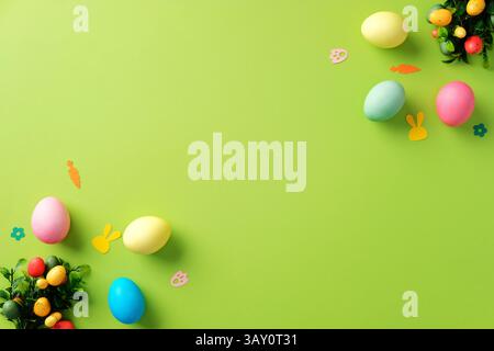 Happy Easter greeting card design. Top view colorful Easter eggs, bunny paper cutouts, and festive decorations on a green background. Stock Photo