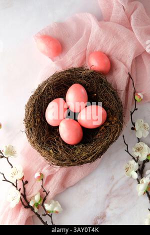 Stylish pink eggs in nest on soft pink cloth with delicate white flowers on cherry blossom branch. Happy Easter concept. Stock Photo