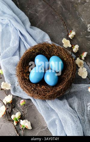Blue Easter eggs in nest, cherry blossom twigs, and blue fabric on stone background. Happy Easter concept Stock Photo