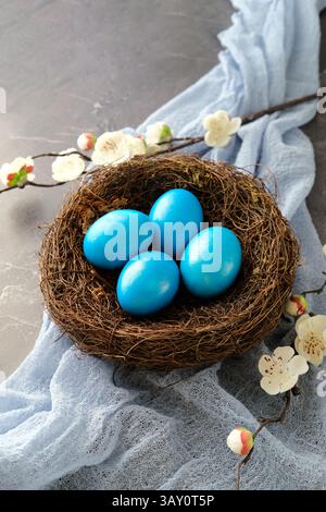 Blue Easter eggs in a nest with white cherry blossoms, set against a soft blue fabric Stock Photo