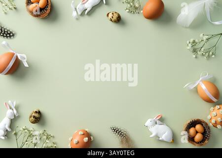 Happy Easter greeting card design. Flat lay composition with decorated Easter eggs, ceramic bunnies, flowers on pastel green background. Stock Photo