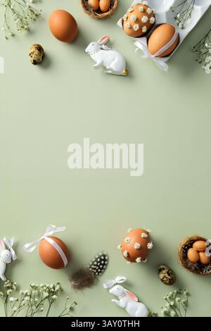 Elegant Easter flat lay composition with decorated brown eggs, ceramic bunnies, and flowers on a light green background. Stock Photo