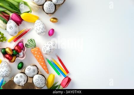 Colorful Easter scene with eggs for coloring, tulips, chocolate eggs, and markers on a white background. Easter eggs for kids coloring DIY concept. Stock Photo