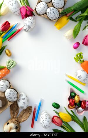 Easter flat lay with colorful decorated eggs, tulips, chocolate candies, and painting supplies arranged around a blank white space. DIY, handicraft Ea Stock Photo