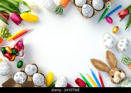 Easter flat lay with eggs for coloring, colorful tulips, felt-tip pens, chocolate candies, and craft supplies on a white background. Stock Photo