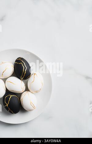 Stylish golden and black Easter eggs in plate on marble table. Flat lay, top view. Happy Easter vertical banner Stock Photo