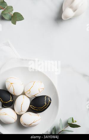 Happy Easter concept. Luxury Easter eggs, bunny rabbit, eucalyptus leaves on marble table. Flat lay, top view, vertical. Stock Photo