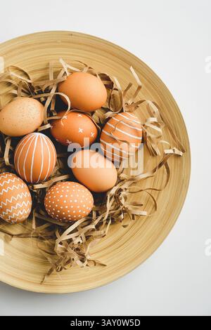 Easter eggs and straw on plate on white background. Flat lay, top view, vertical Stock Photo