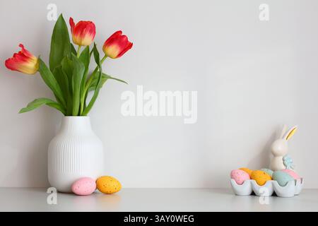 Happy Easter composition. Table with vase of tulips, colorful Easter eggs, decorative bunny. Stock Photo