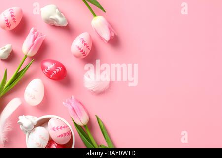 Happy Easter greeting card template. Colorful Easter eggs, tulips flowers on pink table. Top view, flat lay. Stock Photo