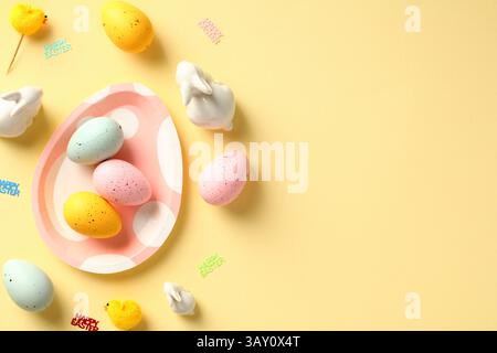 Happy Easter greeting card. Cute plate with colorful Easter eggs, decorative Easter rabbits, chickens on pastel yellow background. Stock Photo