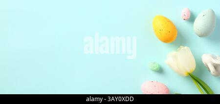 Happy Easter banner with space for text. Colorful Easter eggs, white tulip, Easter bunny on pastel blue background. Stock Photo