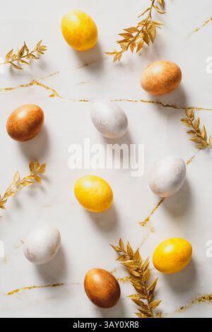 Happy Easter flat lay composition. Easter eggs and golden leaves on marble table top view. Stock Photo