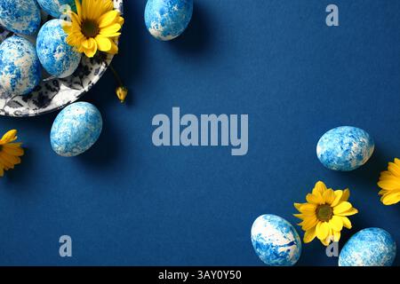 Blue and white Easter eggs on dark blue background with yellow flowers. Top view. Stock Photo