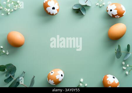 Happy Easter card design. Frame made of Easter eggs, eucalyptus leaves and flowers on pastel green background. Stock Photo