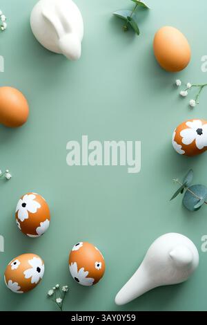 Easter flat lay vertical composition. Easter eggs, flowers, Easter bunny on pastel green background. Stock Photo