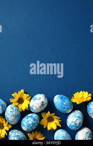 Easter poster, vertical banner design. Blue and white Easter eggs with yellow flowers on dark blue background. Top view. Flat lay. Stock Photo