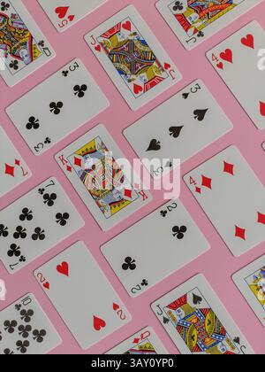 playing cards arranged against a pink background. The cards are laid out in a repeating pattern, featuring a mix of different suits and values. Stock Photo