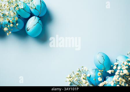 Elegant Easter eggs with white flowers on pastel blue background. Flat lay, top view, copy space. Stock Photo
