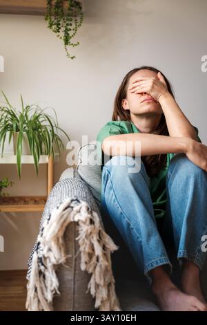Exhausted woman sitting on sofa with hand covering her face at home Stock Photo