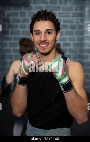 Young boxer smiling while displaying bandaged hands during training in a gym, embodying strength and dedication in his workout routine Stock Photo