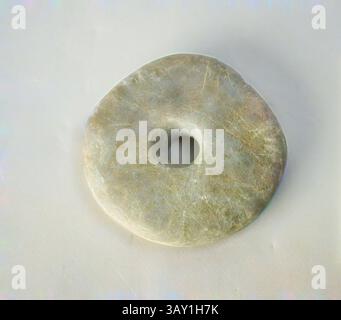 A smooth, circular stone pendant with a central hole, displaying natural variations in texture and color., Unknown (English), Mace head, Granite, 3 1/4 x 1 1/4 in., Classic art with a modern twist reimagined by Artotop Stock Photo