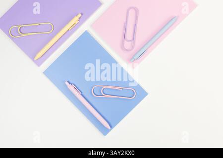 Top view of pink, purple and blue notebooks on white background. Pink, yellow and blue pens, paperclips, school, office wallpaper. Flat lay, copy spac Stock Photo
