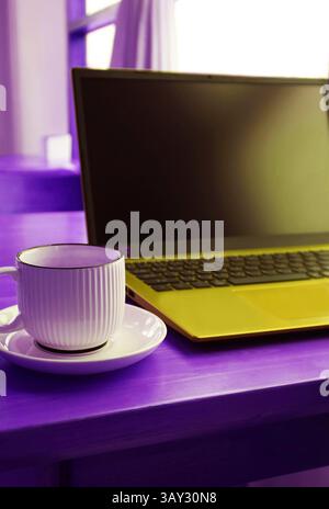 Pop Art Style of Ultramarine Mustard Yellow Opened Laptop with a Coffee Cup on Purple Table Stock Photo