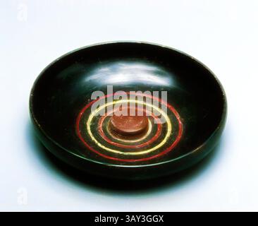 A circular bowl with a smooth, dark exterior and a central round element, featuring concentric rings in red and yellow that create a striking visual contrast. The design showcases a blend of simplicity and elegance, highlighting craftsmanship., Greek, Phiale, late 6th Century BC, glazed earthenware, height by diameter: 1 1/4 x 6 in., Classic art with a modern twist reimagined by Artotop Stock Photo
