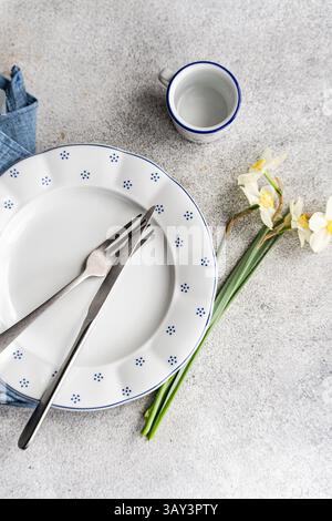 Top view of a minimalist breakfast setting featuring an empty plate with blue polka dots, a matching cup, cutlery, and white daffodils, all arranged o Stock Photo
