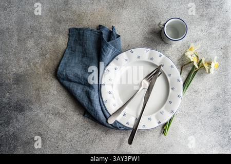 From above view of a stylish table setting featuring a white ceramic plate with blue dots, silver cutlery, a blue napkin, a small white cup, and white Stock Photo