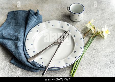 From above, a dining setup featuring a white plate with blue polka dots, accompanied by silverware on a blue napkin and a matching cup. Beside the pla Stock Photo