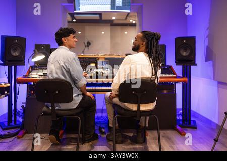 Two men collaborating in a professional recording studio, surrounded by audio equipment and ambient blue lighting. Perfect for depicting a creative mu Stock Photo