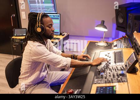 A focused audio engineer wearing headphones operates advanced mixing equipment in a modern recording studio environment, capturing the essence of musi Stock Photo