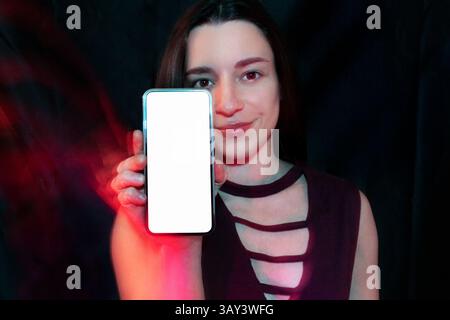 A woman holds a smartphone with a blank white screen against a dark background. The image has a vibrant, colorful lighting effect, emphasizing the mod Stock Photo