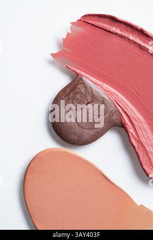 High-resolution image showcasing assorted cosmetic textures. The photo includes a swipe of red lipstick, a bronze eyeshadow, and a beige foundation ap Stock Photo