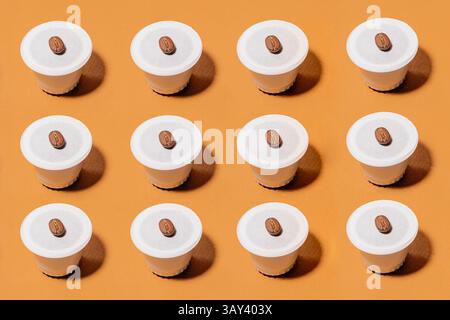 A neatly arranged grid of biodegradable coffee pods, each topped with a coffee bean, set against a vibrant orange background. The image highlights sym Stock Photo