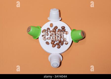 A creative flat lay of biodegradable coffee capsules encircling coffee beans on a white base against an orange background. The arrangement highlights Stock Photo